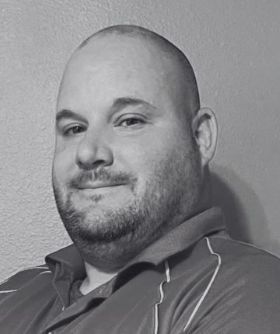 Black and white portrait of a bald man with a beard wearing a collared polo shirt