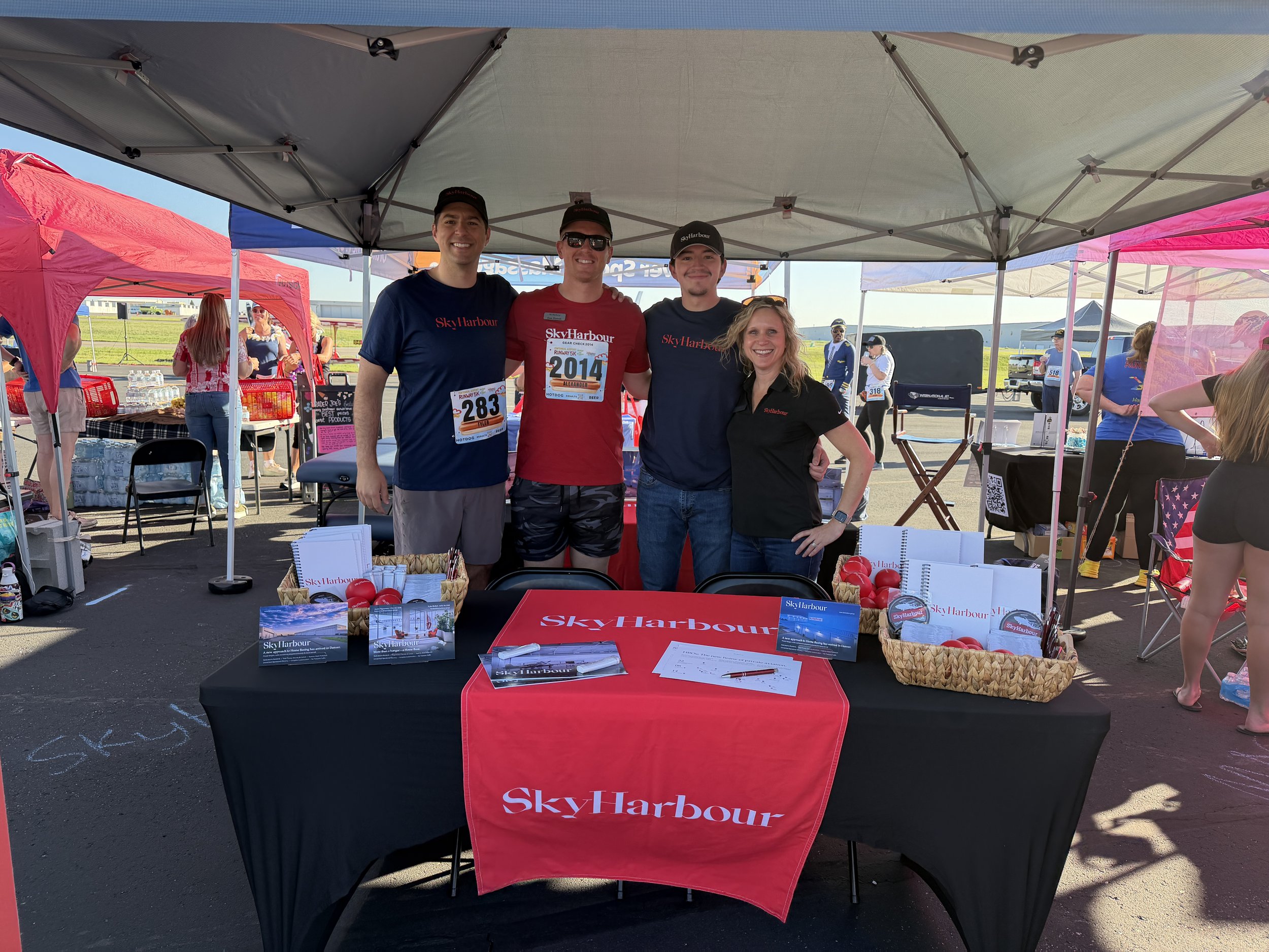 Group of people at a Sky Harbour event booth with a red tablecloth under a tent