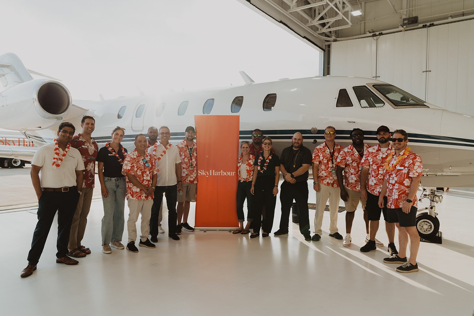 Group of people in matching Hawaiian-style shirts standing in front of a private jet inside a hangar