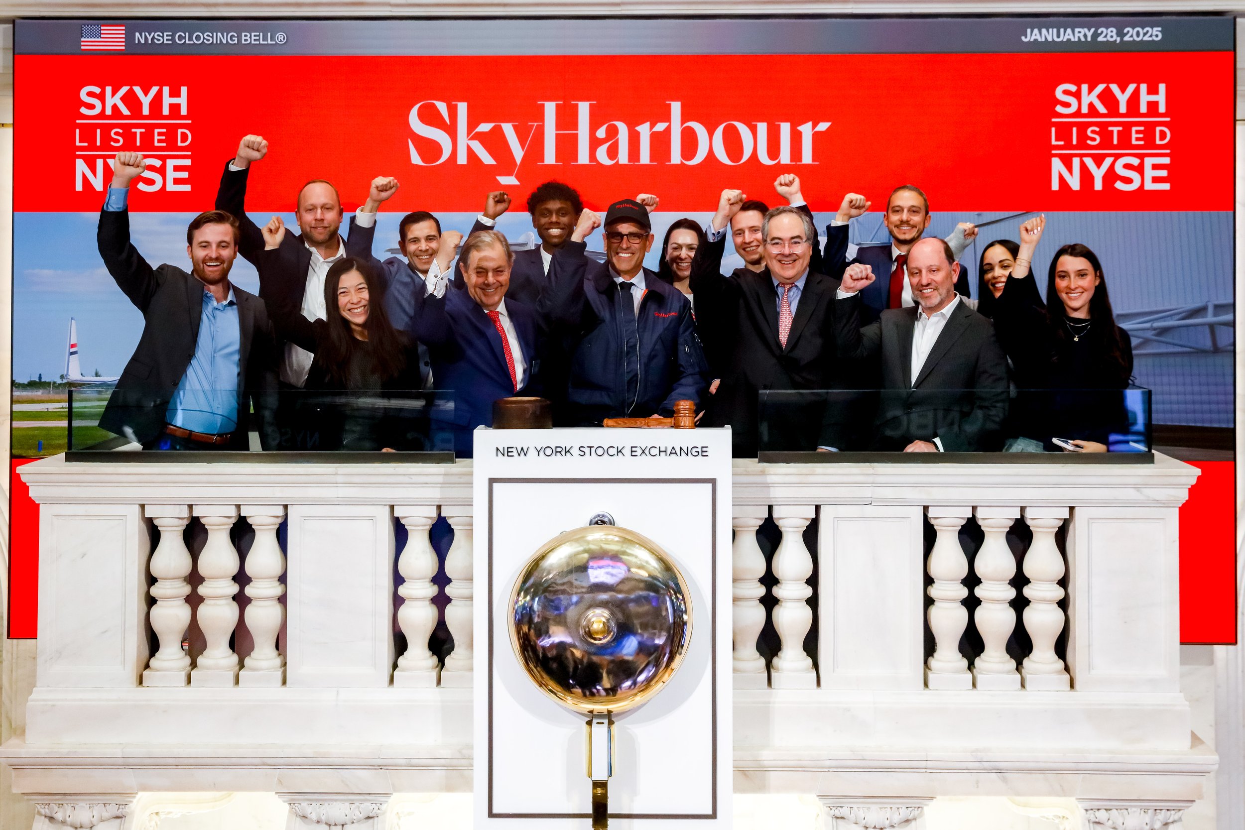 Group of people celebrating behind a podium at the New York Stock Exchange under SkyHarbour SKYH listed banners