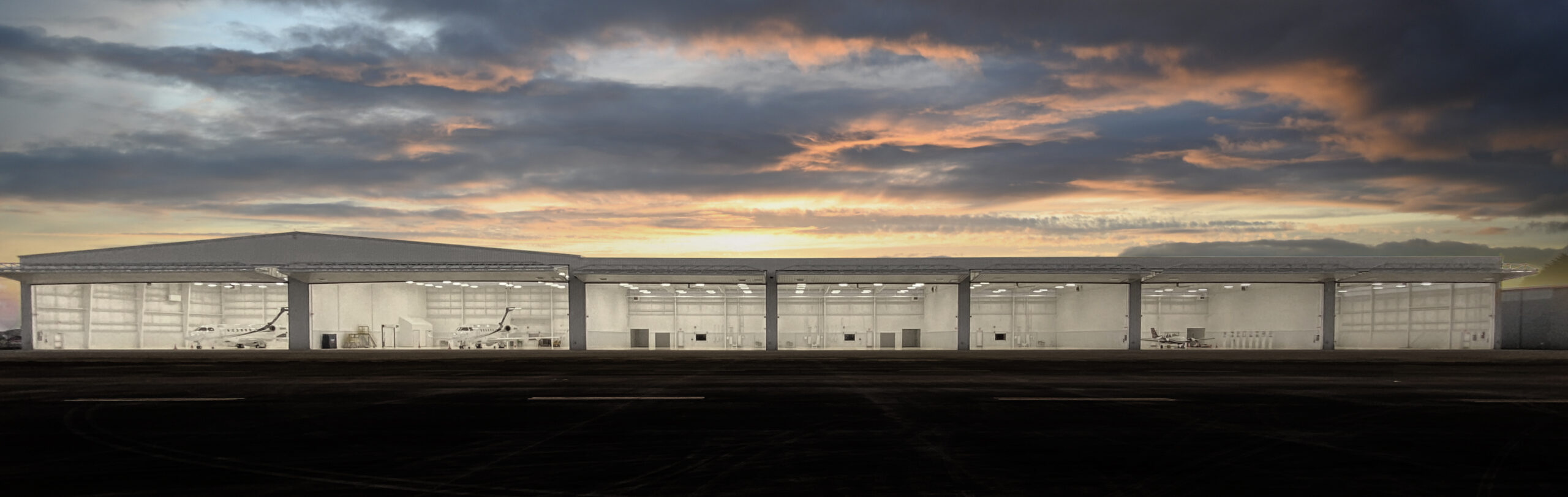 Panoramic view of a long hangar building under a dramatic sunset sky
