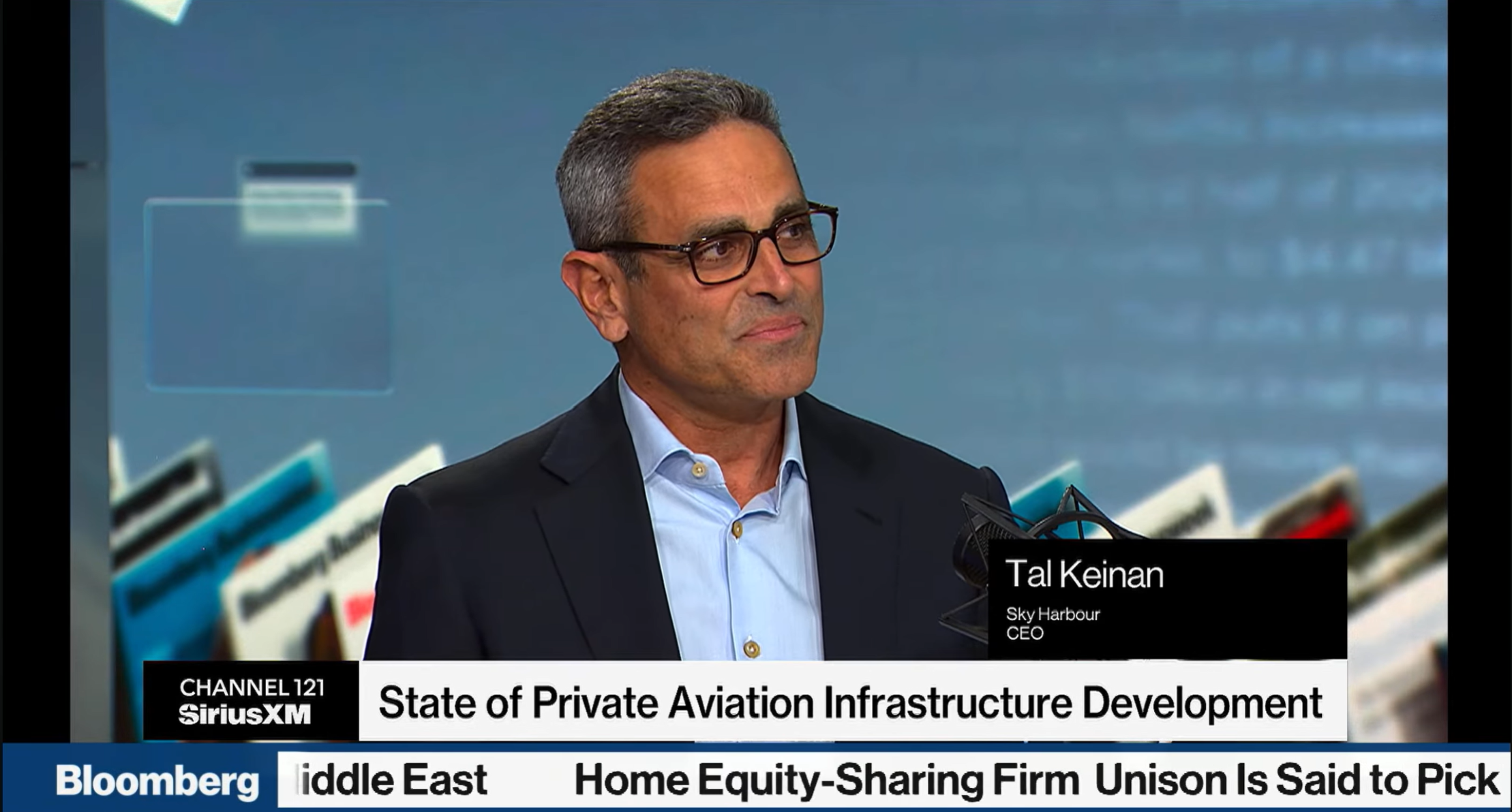 Man in glasses and a dark blazer speaking on a Bloomberg broadcast titled State of Private Aviation Infrastructure Development